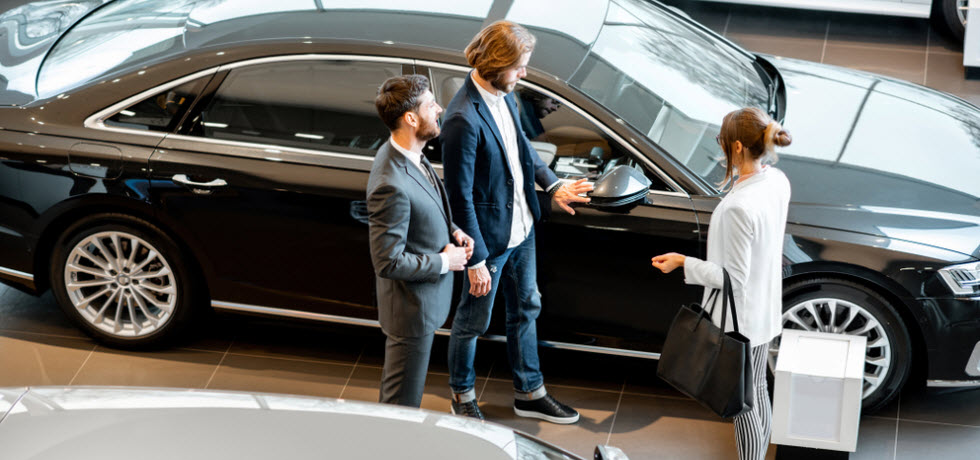 Car salesman showing a new car in a car showroom to a business couple