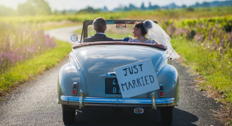 A newlywed couple driving in retro car in the countryside