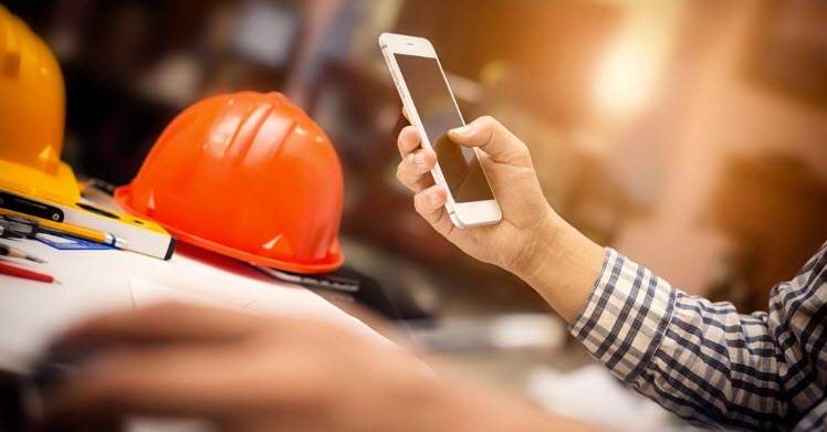 construction office desk and holding mobile smartphone