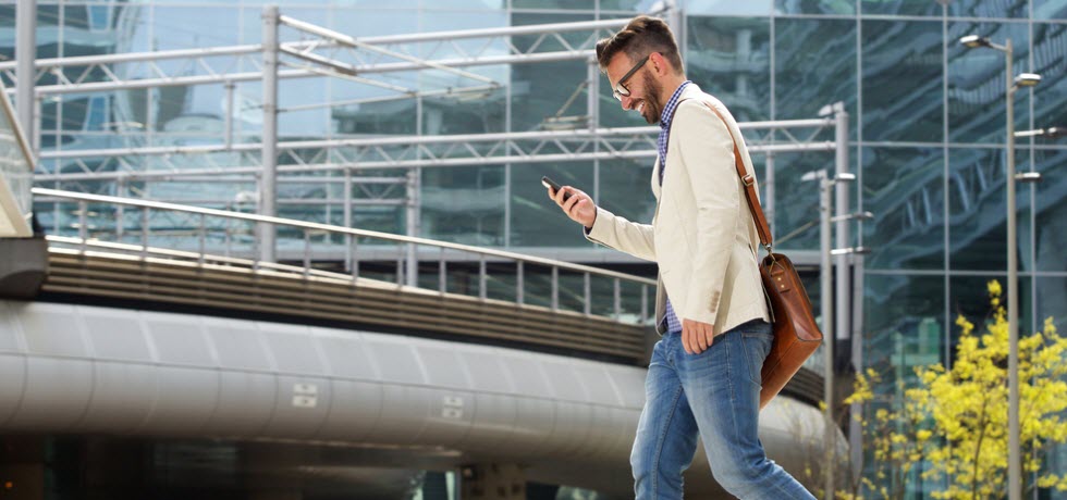 Man walking outdoors and reading a text message on his mobile phone