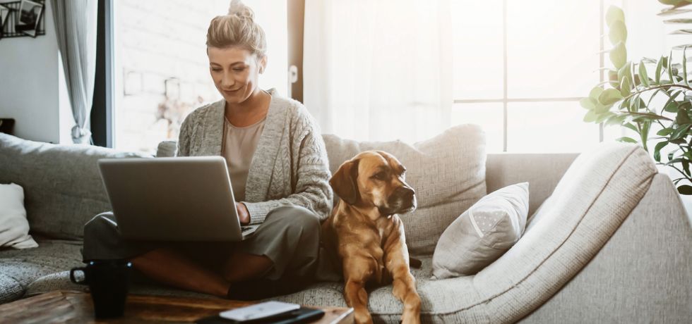 a woman laptop on her knees working at home with a dog sitting next to her